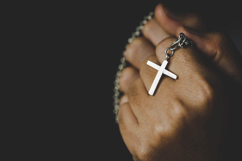 Person holding a crucifix and chain in their fist.